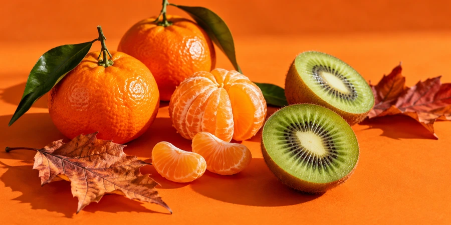 Clémentines, kiwis coupés et feuilles d’automne sur un fond orange vif